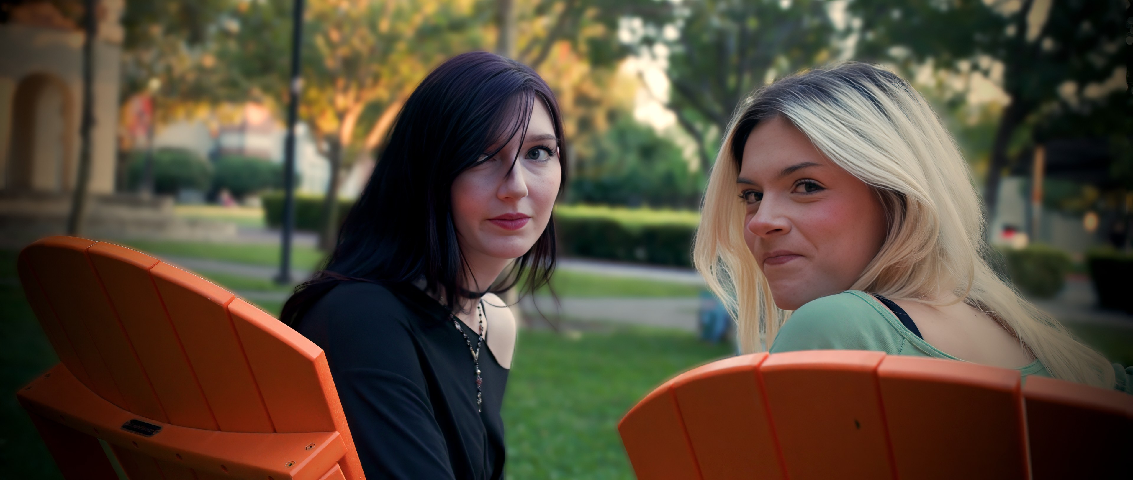Two students seated on a campus lawn, turning to look back